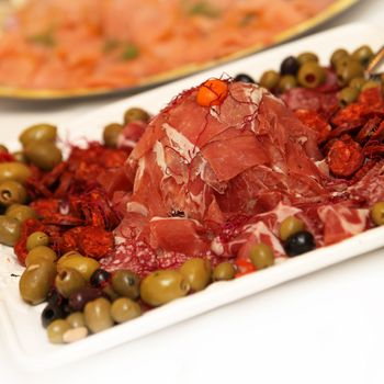 Ham and salami on a plate decorated with olives