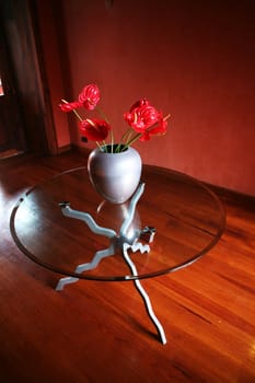 Small glass table with red flowers in vase in warm wooden interior