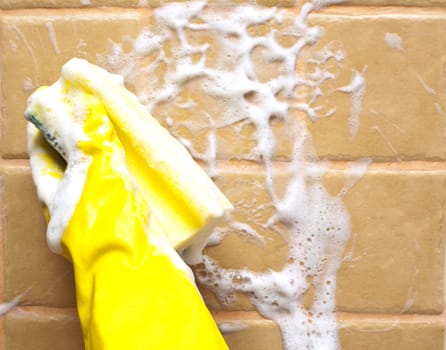 hand in yellow rubber glove holding soapy cleaning sponge 