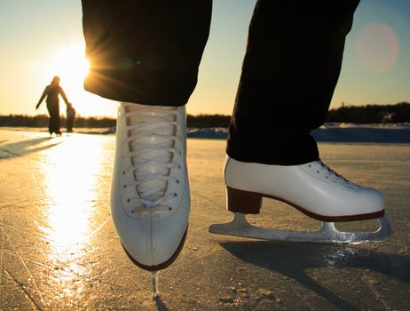 Ice skating. Ice skates in action closeup outdoors. Classic figure ice skates on frozen lake outdoors in evening light, Mom and daughter silhouette in the background. Lac Beauport, Quebec City, Canada.