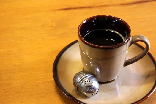 A tea strainer sitting next to a mug of hot freshly brewed tea.
