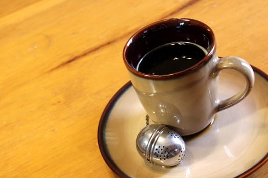 A tea strainer sitting next to a mug of hot freshly brewed tea.
