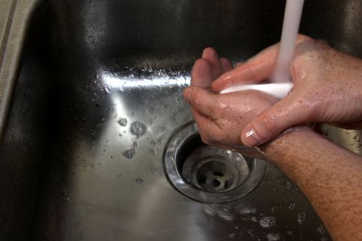 A man washing his hands with soap in a sink.
