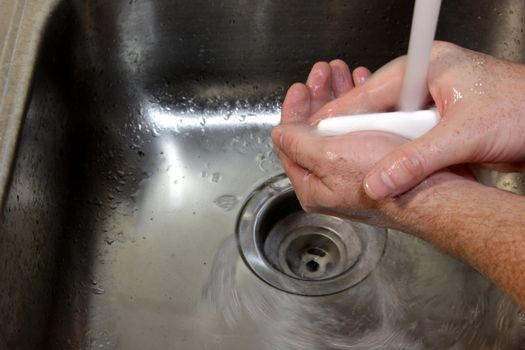A man washing his hands with soap in a sink.
