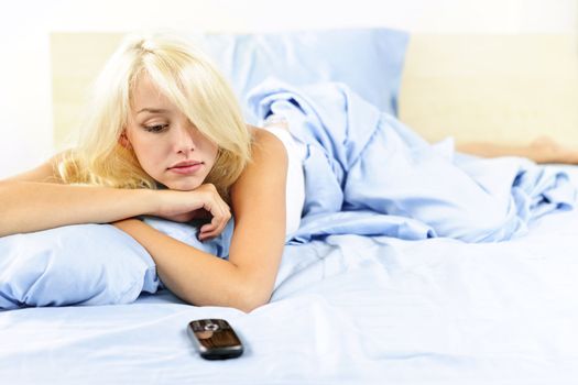Sad blonde woman waiting for phone call in bed at home