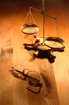 Ancient brass weight scale standing near old spectacles on nice wooden background