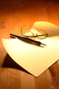 Old spectacles and ink pen lying on blank sheet of paper on wooden background