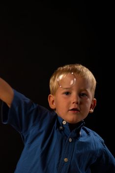 Blond boy concentrated trying to catch a soap bubble