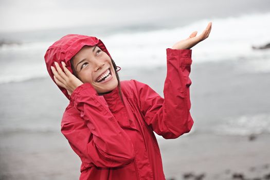 Woman in red raincoat enjoying the rain and having fun outside on the beach on a gray rainy autumn day. Asian / Caucasian model.  