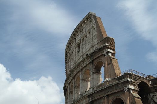 Daytime image of the Roman Coliseum with bright sun and partly cloudy skys.