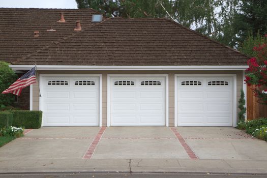 Beige three ar garage with white doors and brick and red brick driveway