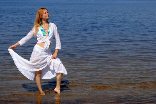 Pretty girl in white summer dress dancing in water.