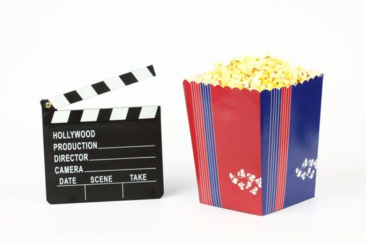 Movie clapper board and box of popcorn over white 