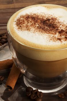 cappuccino with chocolate powder on milk froth and cinnamon sticks on wooden background