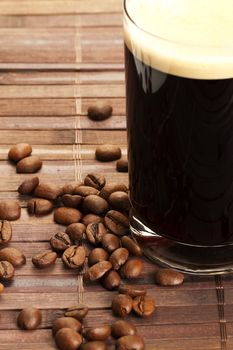 coffee beans near black coffee in a straight glass on wooden background