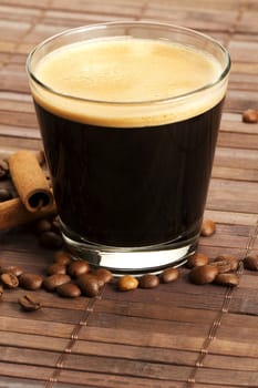 espresso in a short glass with coffee beans and cinnamon sticks from diagonal top on wooden background