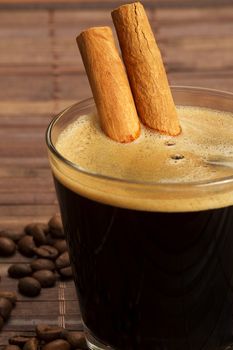 cinnamon sticks inside espresso in a short glass coffee beans aside on wooden background