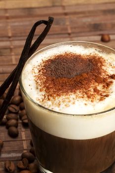 coffee with milk froth, cocoa powder and standing vanilla beans on wooden background with coffee beans