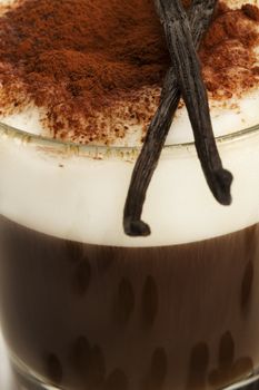 closeup on coffee with milk froth and chocolate powder with vanilla beans on top