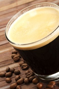 black espresso coffee in a short glass with coffee beans on wooden background