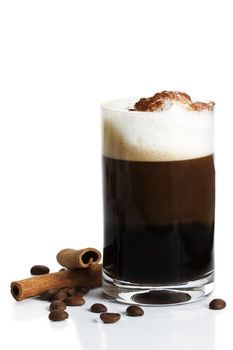 espresso in a straigt glass with milk froth cocoa powder, cinnamon sticks and coffee beans aside on white background