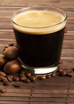 espresso coffee in a short glass with hazelnuts and coffee beans on wooden background