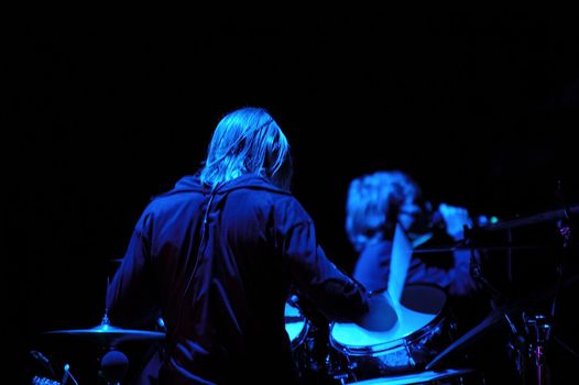 Drummer is playing in a band. The light setting is blue. Note the stick is in motion blur.