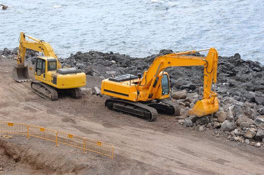 Two orange excavators near the sea