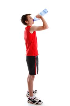 A teenage boy dressed in sports wear is drinking water from a bottle.  White background.