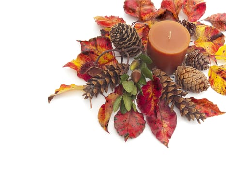 Still life of orange candle amidst colorful Fall leaves and pine cones isolated on white. Corner design allows for plenty of copy space.