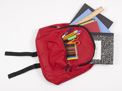 Back-to-school concept. Overhead shot of red backpack stuffed with student books, colored pencils, markers, pens, and scissors.