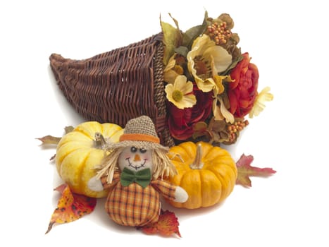 Still-life of Thanksgiving craft objects: handsewn scarecrow doll, miniature pumpkins, and silk flowers in a cornucopia basket. Isolated on white.