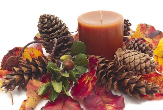 Colorful still life with deep orange pillar candle among brilliant autumn leaves, pine cones, and acorn. All on white background.