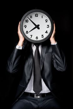 man in gray suit holding big clock covering his face