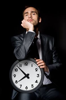 bored businessman holding clock, over black