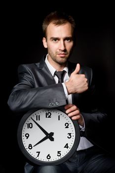 handsome business man holding clock, showing his thumb up