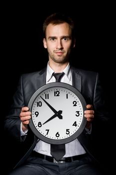 young handsome businessman holding clock, over black