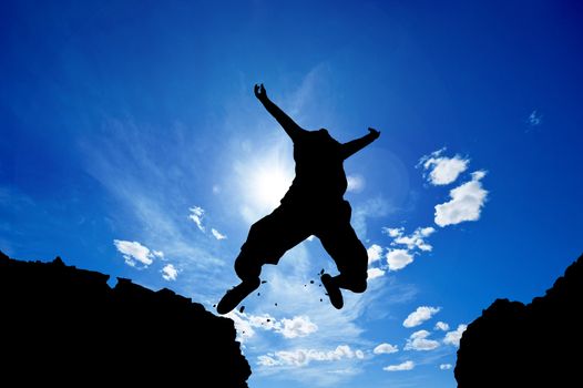 man jumping from a cliff over vivid blue sky