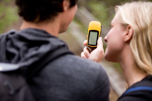 A couple outdoors in the forest using a GPS.  Sharp focus on the GPS device.