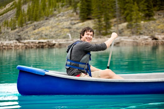 A portrait of a smiling man in a canoe on a glacial lake