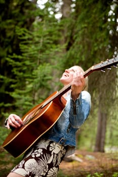 A woman singing freely in the forest with a guitar - sharp focus on guitar
