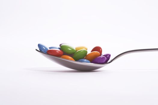 spoon with colorful sweets over white background