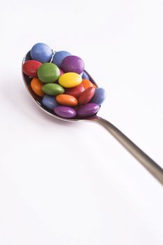 spoon with colorful sweets over white background