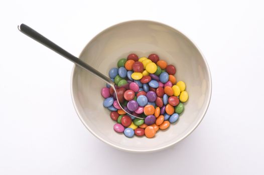 bowl with spoon and colorful sweets over white