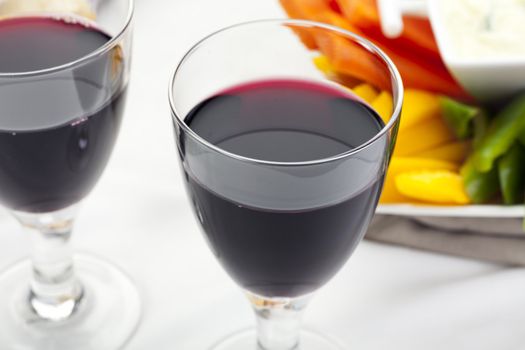 Glass of red wine on table with appetizers in background.