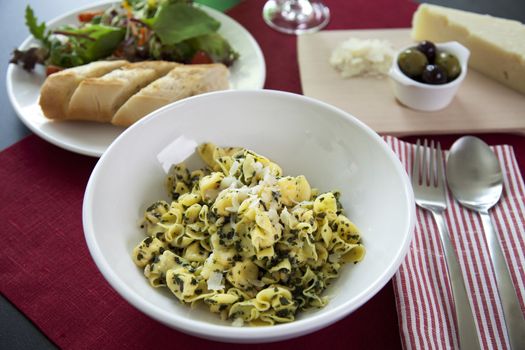 Perline pasta with pesto sauce on table with salad and olives.