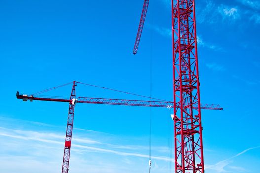 Closeup of two red tower construction cranes against blue sky