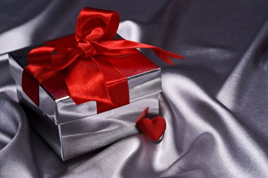 valentine gift with decorative red ribbon on silver silk background
