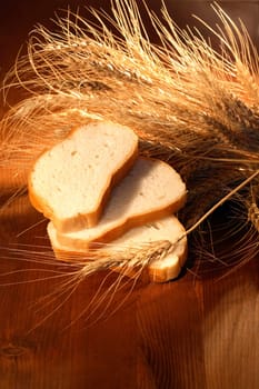 Still life with white sliced bread and ears of wheat on wooden background