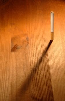 One cigarette standing on wooden background with long shadow